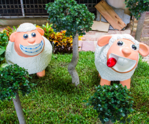 Cherry white garden sheep statues with with big smiles and bright eyes standing in a garden.