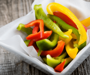 Freshly sliced red, green and yellow bell peppers in a white dish.