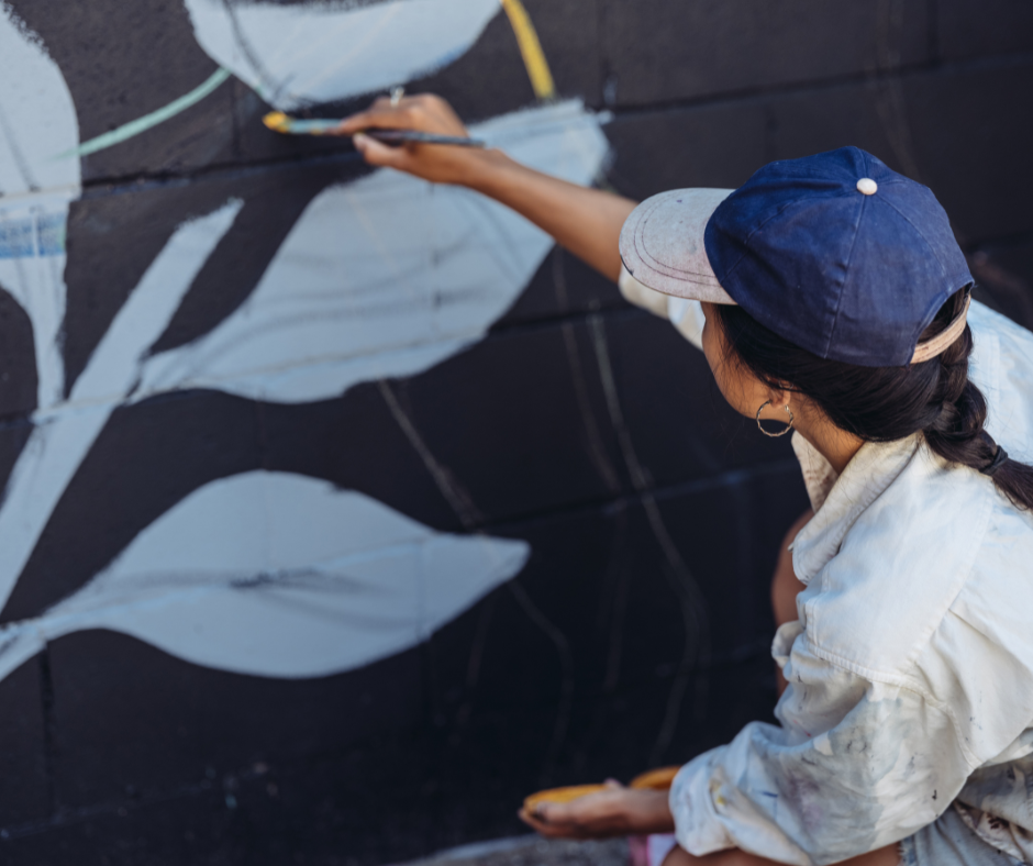 Woman painting a black and while mural on a garden wall.