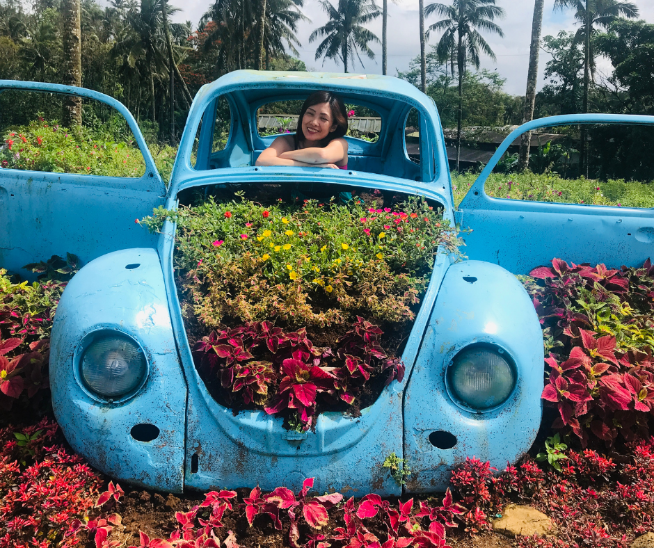 A woman posing for a picture inside an old blue VW Bug turned in to a whimsical garden planter.
