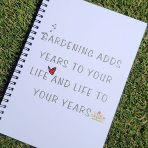 A white spiral notebook with the words " Gardening adds years to your life and life to your years" on the cover.