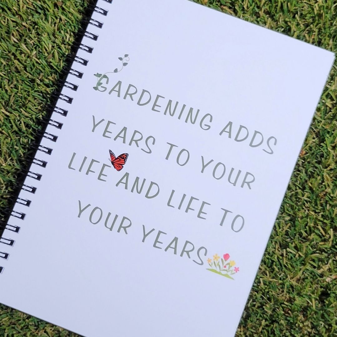 A white spiral notebook with the words " Gardening adds years to your life and life to your years" on the cover.