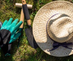 A straw garden hat next to a  gloves and tools on grass.