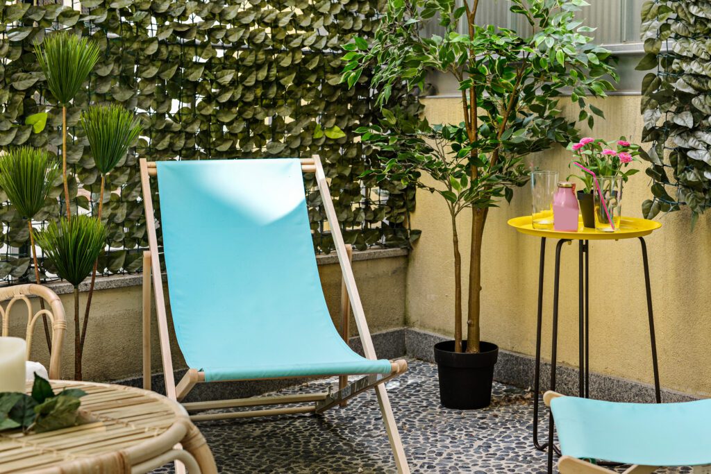 Corner of an urban terrace with wooden hammocks and blue fabric, artificial decorative plants for privacy, and stone floors