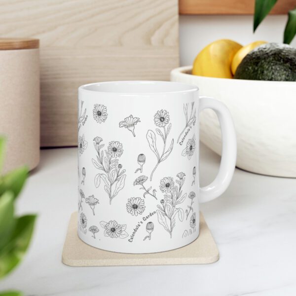 A coffee mug with botanical style calendula flower print on desk.