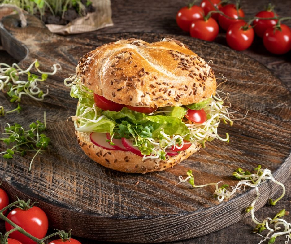 A burger with lots of veggies including broccoli sprouts.