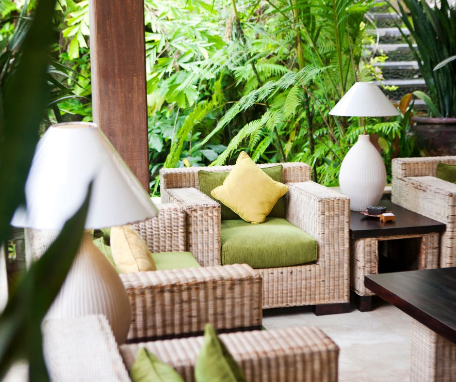 An outdoor living room set of wicker patio furniture and large tropical potted plants.