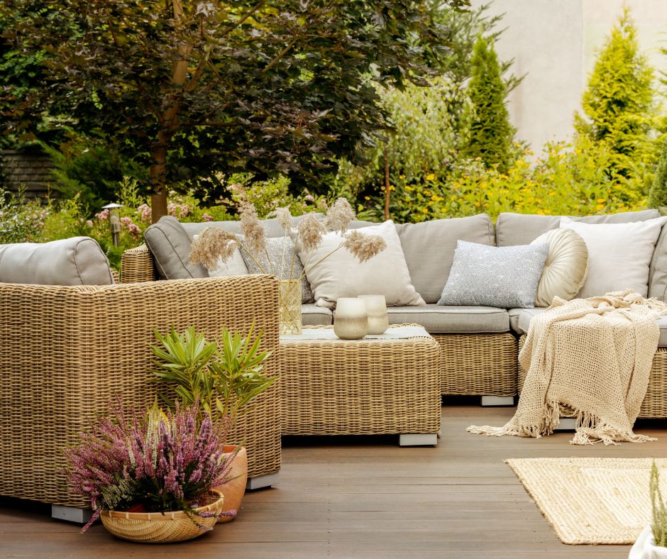 A comfortable wicker outdoor living space shielded by a large planter of flowers, shrubs, and small pots of herbs.