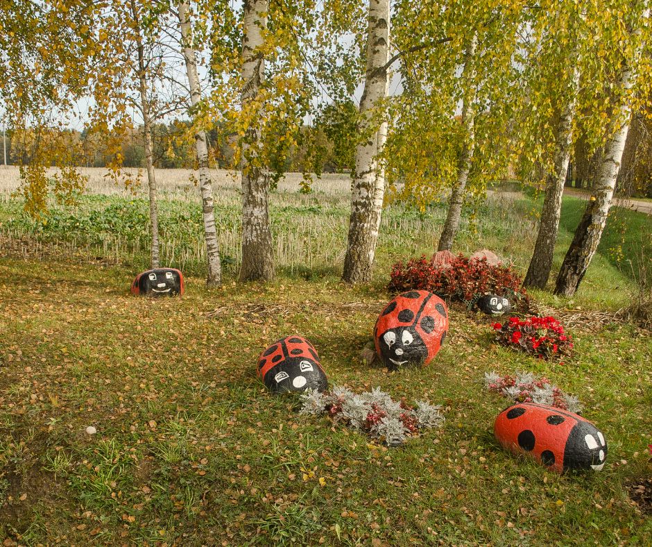 Giant rock with ladybugs painted on them on grass under trees.
