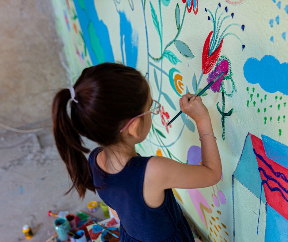 A little girl painting a garden wall mural.