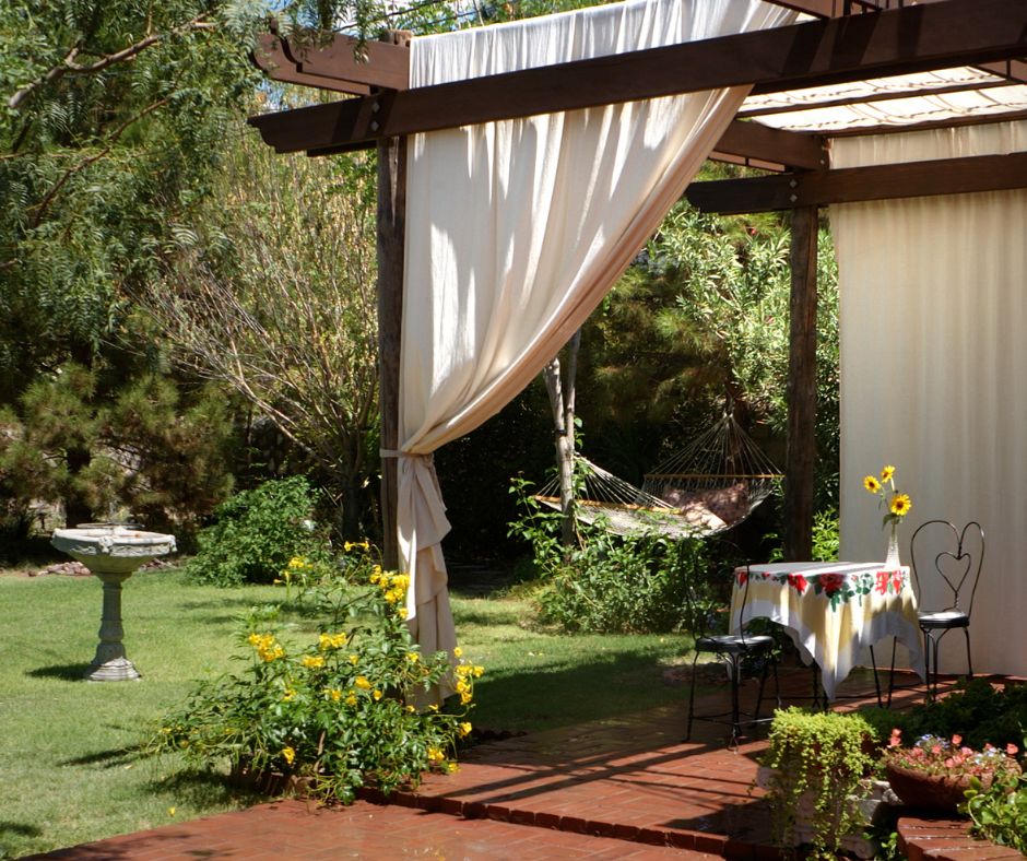 Garden pergola with white outdoor curtains shielding a patio seating area.