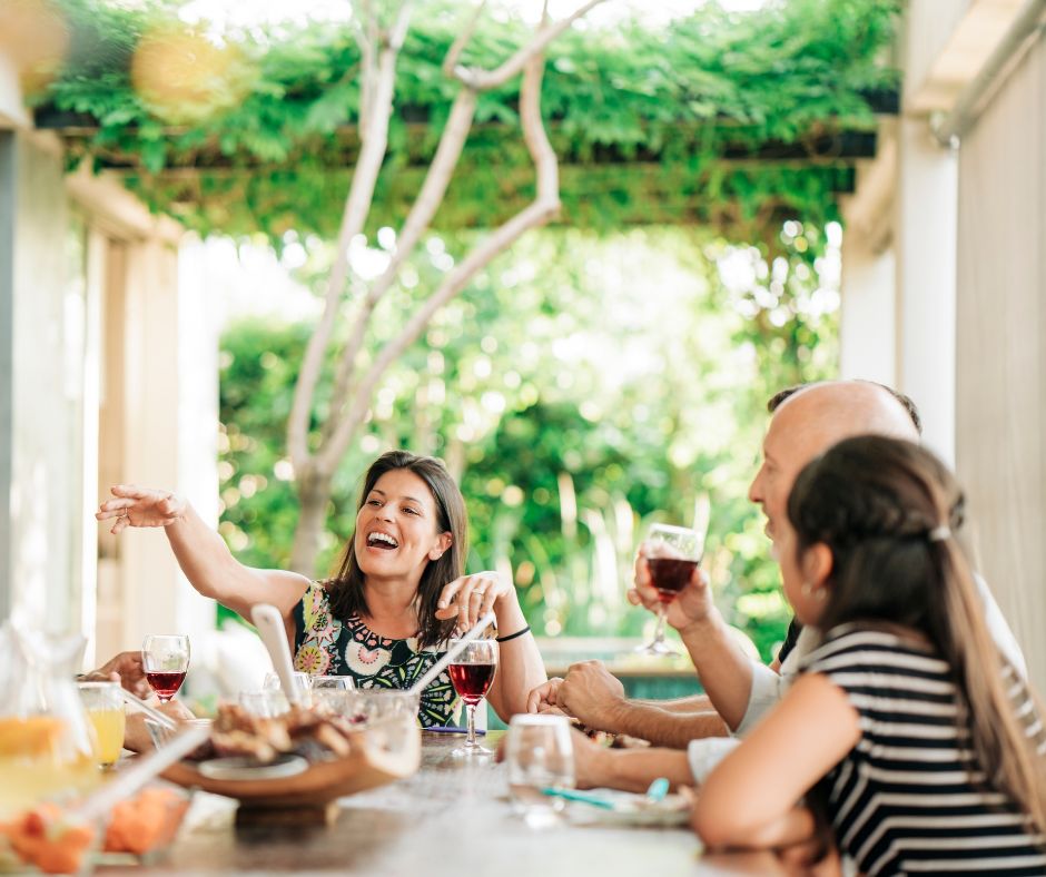 Outdoor curtains being used to provide privacy at an patio party. A woman at the head of the table surrounded by friends and family.