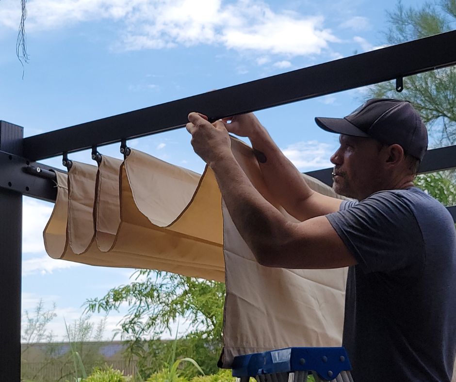 A man installing pergola with a retractable awning and outdoor curtains.