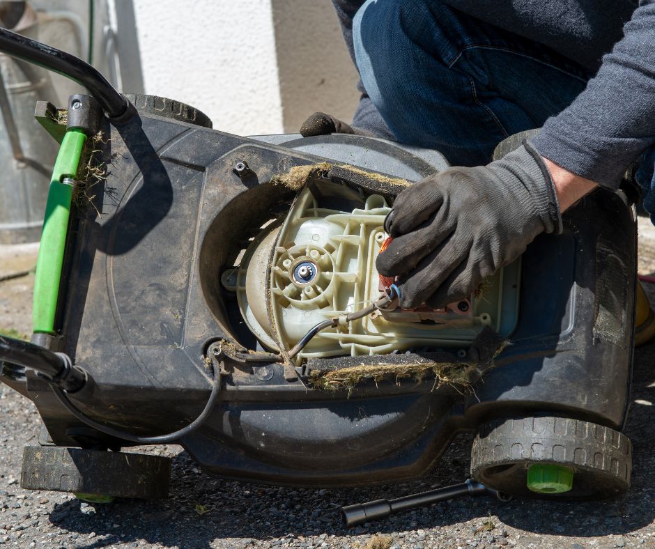 A gloved hand servicing an electric lawn mower to get it ready for winter storage.
