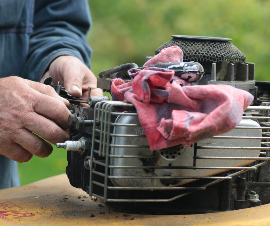 Hands holding tools while working on a lawn mower engine on wood table.