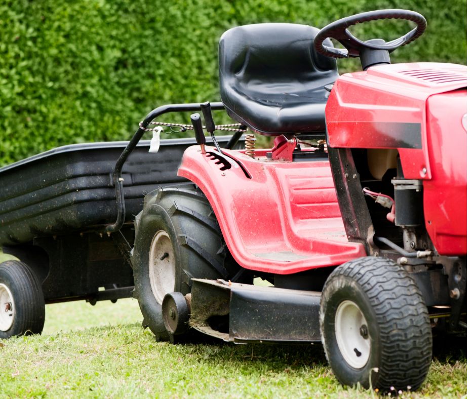 A red riding lawn mower with pull behind cart on cut grass.