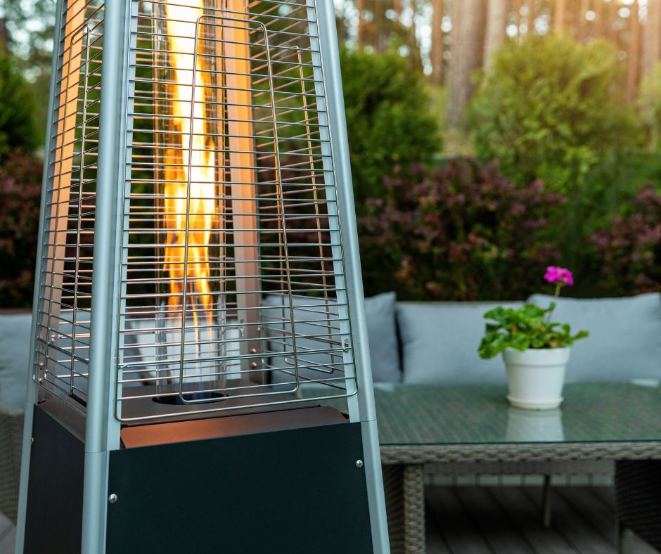 A tall stainless steel propane outdoor heater on a patio with a couch and table.