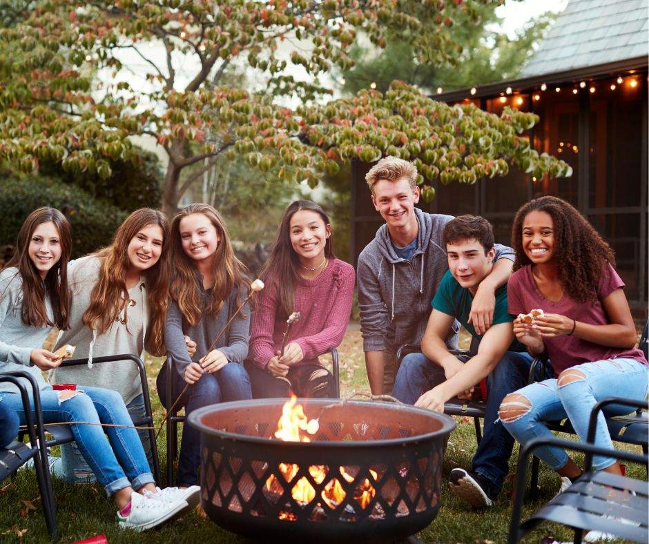 A group of teenagers making s'mores around a fire pit.