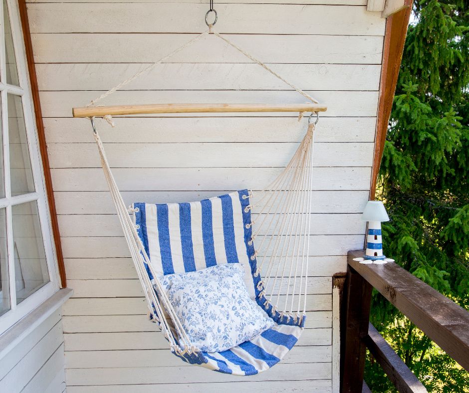 A covered balcony featuring beach decor including a blue and white hammock chair with pillow and a small lighthouse lamp for reading.