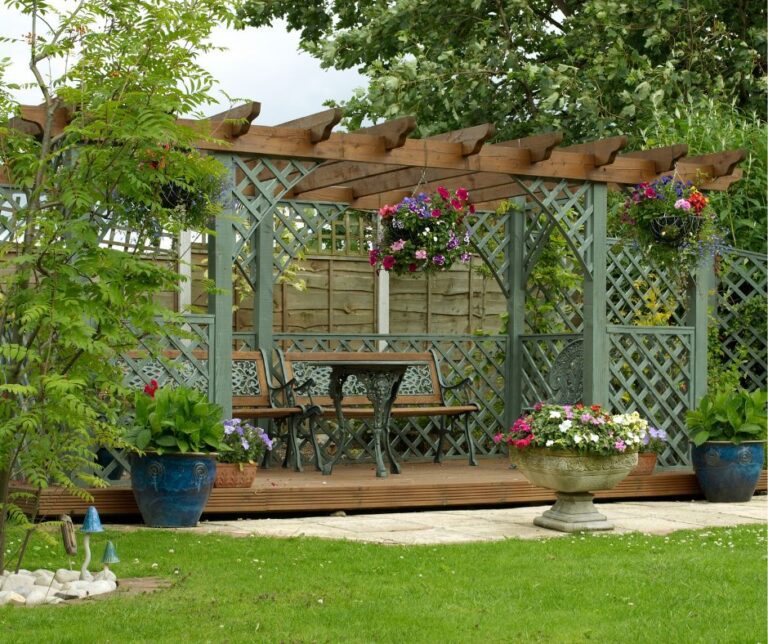 Freestanding pergola with lattice sides in a garden and providing shade to a dinning set.