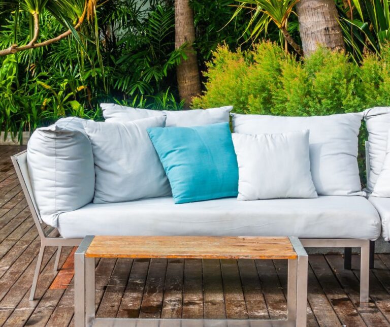 An airy open space coastal style reading space. A soft seafoam blue couch and pillows and light wood table.