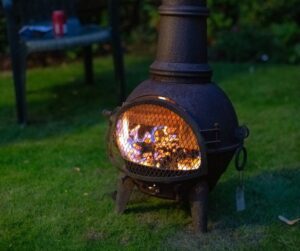 A large black cast iron chimenea with a fire burning inside of with a safety grate in place.