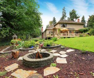 A large stone fire pit a safe distance from a home surrounded  by flagstone.