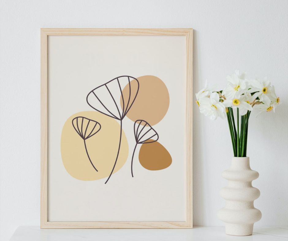 An abstract plant print in neutral tone on a shelf next to a vase of white flowers.