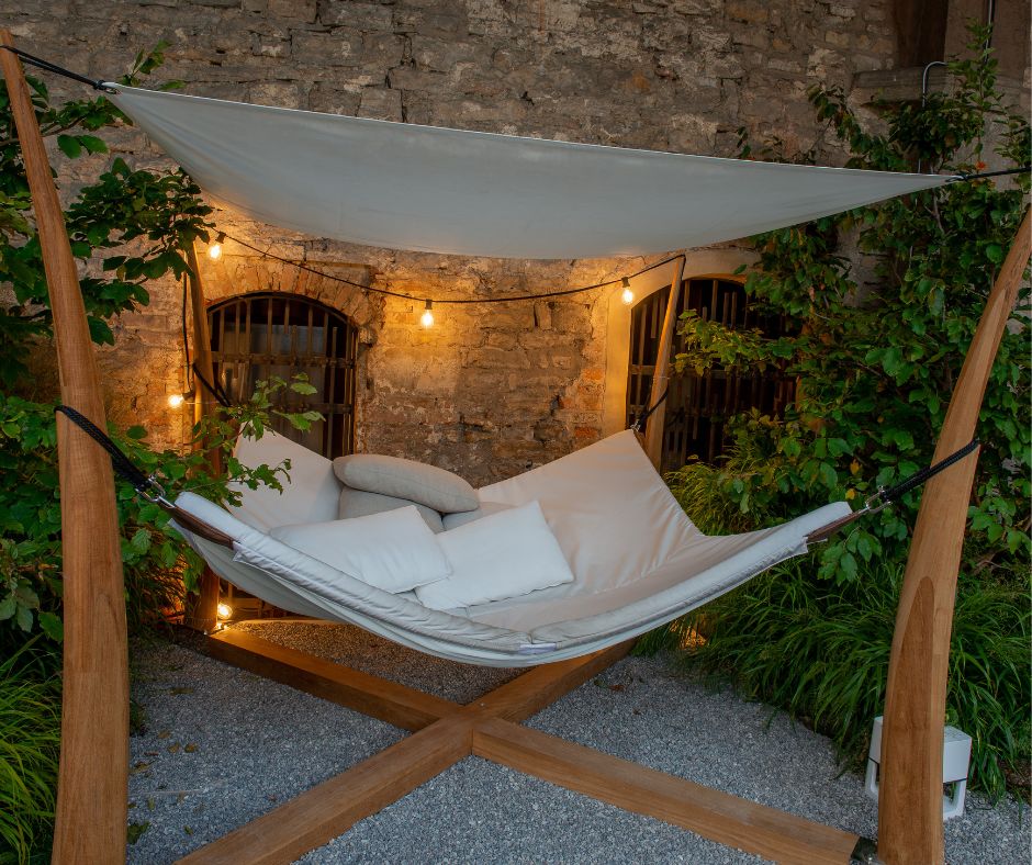 A large custom suspended lounger with a shade cloth. Supports made of a light wood and cushions in a light neutral color.