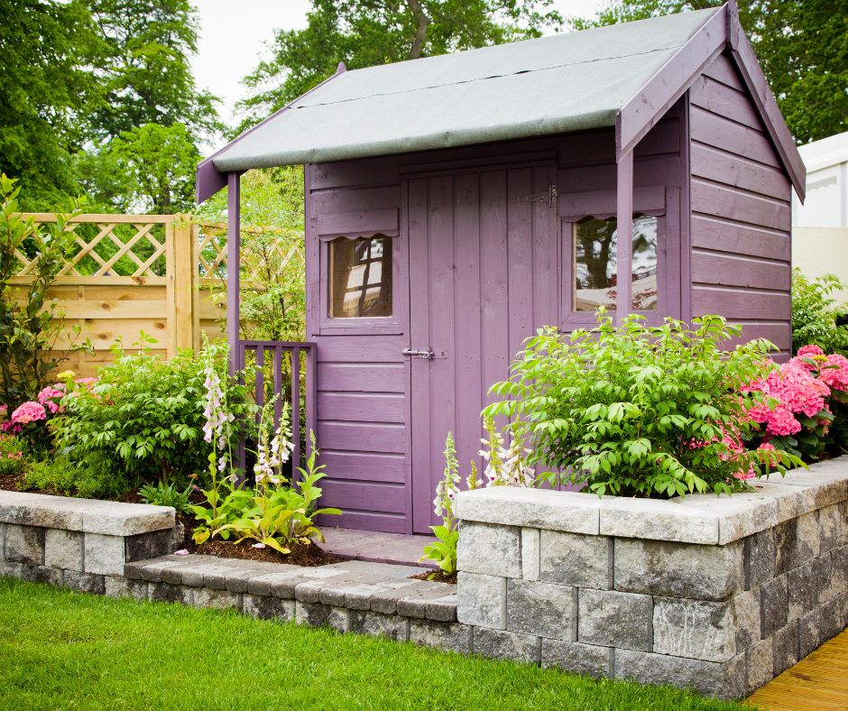A purple mini shed with a covered patio surrounded by lush planter boxes.