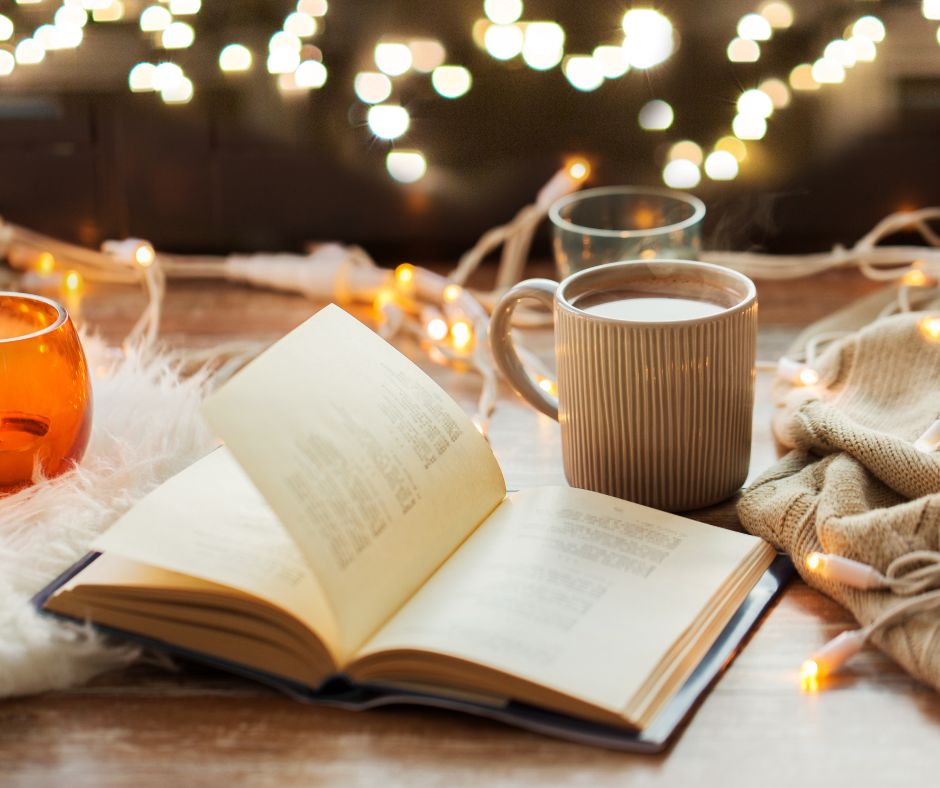 An open book on a table with a steaming mug of coffee and lights.