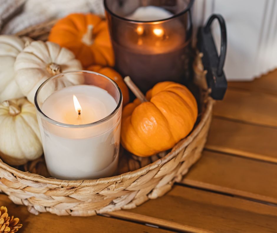 Two container candles in a basket with small white and orange mini pumpkins on a wood table.