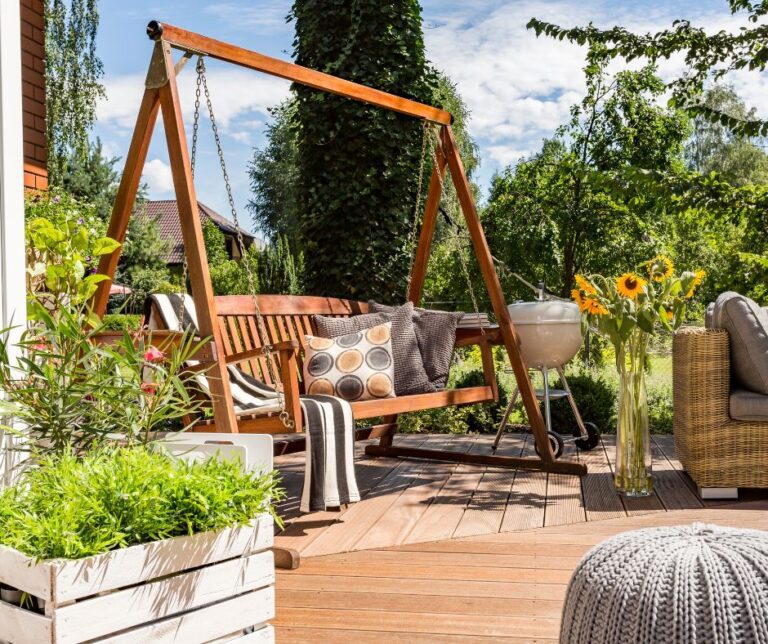 A complete patio set up with planter filled with plants, a wooden swing and a grill.