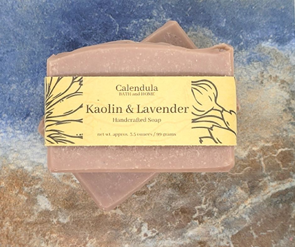 Two bars of a pink botanical soap with a Kraft brown label reading Kaolin & Lavender Handcrafted Soap.