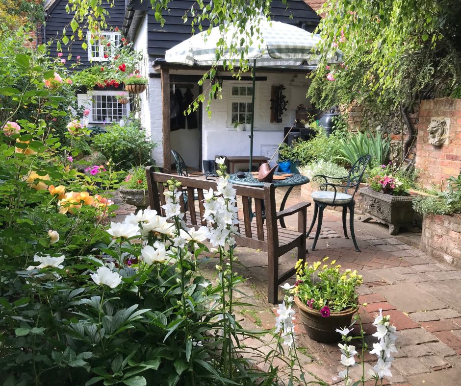 A brick courtyard garden bordered with flowers. A simple sitting areas and a variety of potted plants.