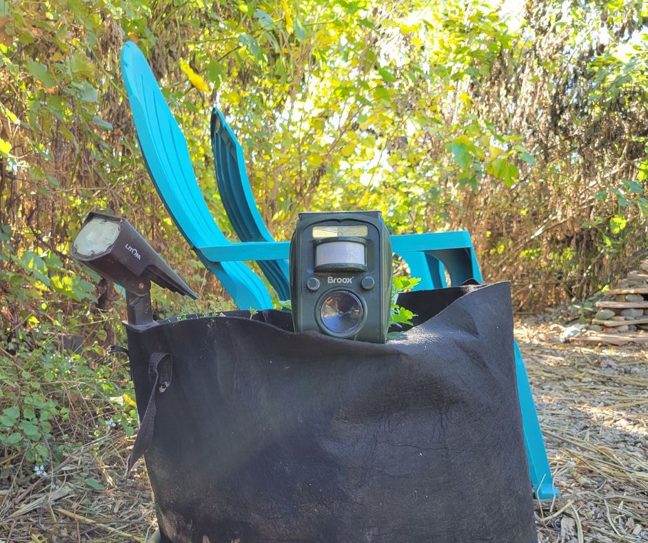 A Green Broox ultra sonic solar animal repellent in a black grow bag.