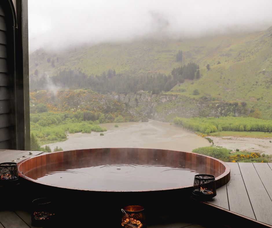 A secluded wooden hot tub built into a deck overlooking a river gorge and forest.