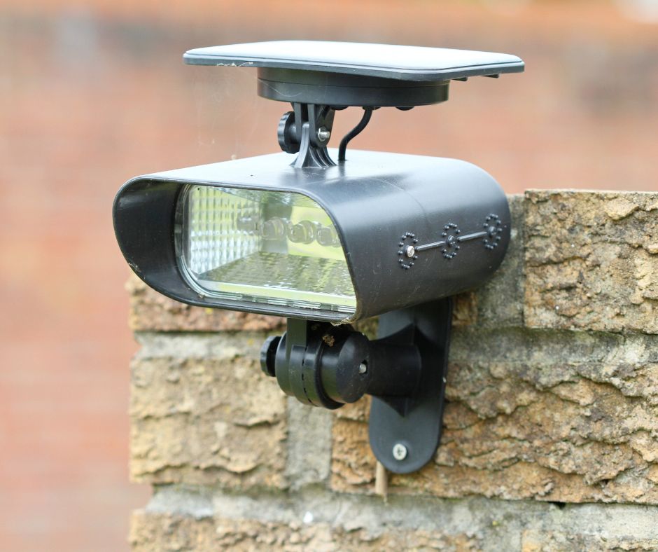 A black motion activated solar spot light mounted on a stone wall used to keep dogs out of the garden.