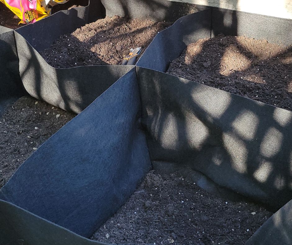 A black partially filled rectangular grow bed style grow bag with built in dividers.