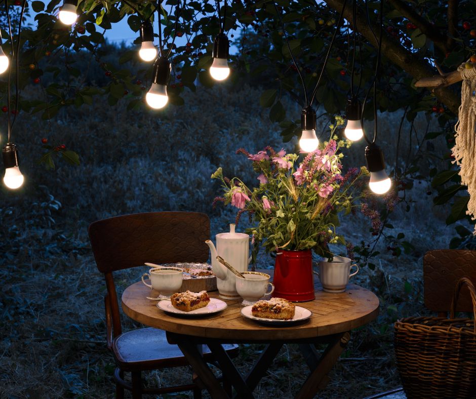 String lights with large bulbs hanging from a tree over a seating for two.