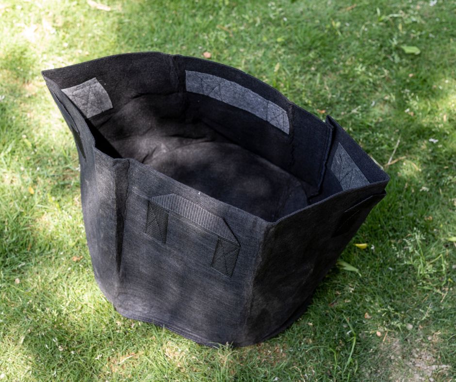 A black empty garden grow bag on a lawn.