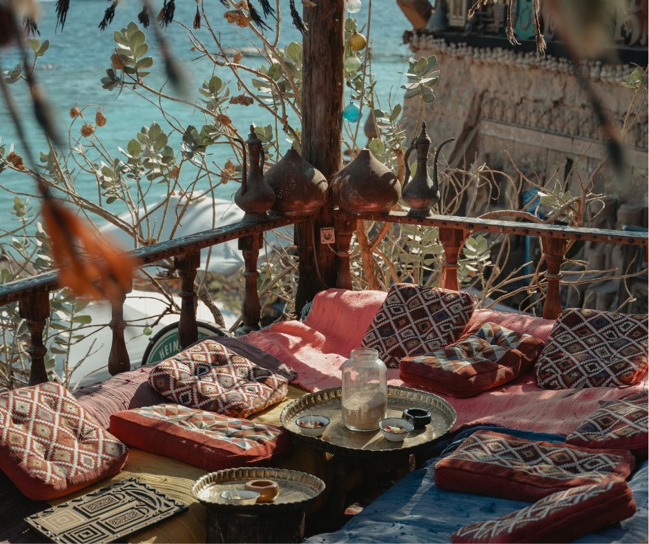 A classical bohemian style seating area featuring warm colors in bold patterns on a balcony overlook water surround by foliage.