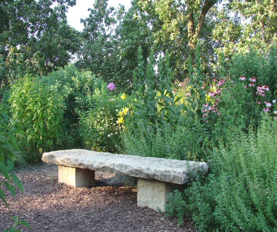A stone garden bench surrounded by flowers and herbs.