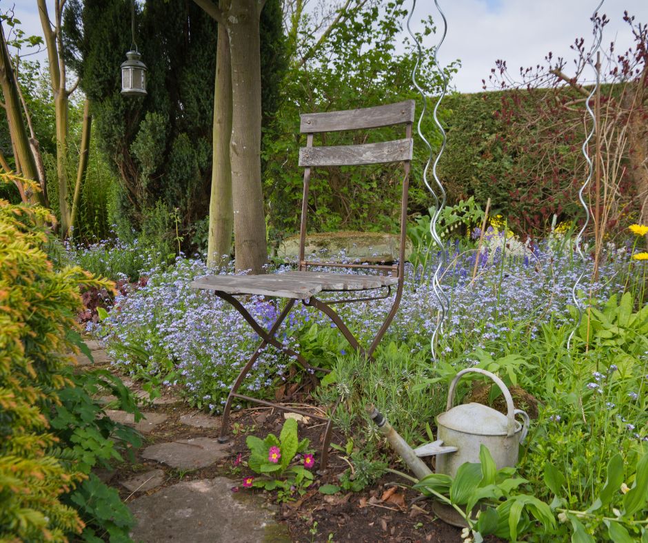 A chair in an insectary garden with a very diverse grouping of plants that attract beneficial insects with yellow, pink and blue flowers.
