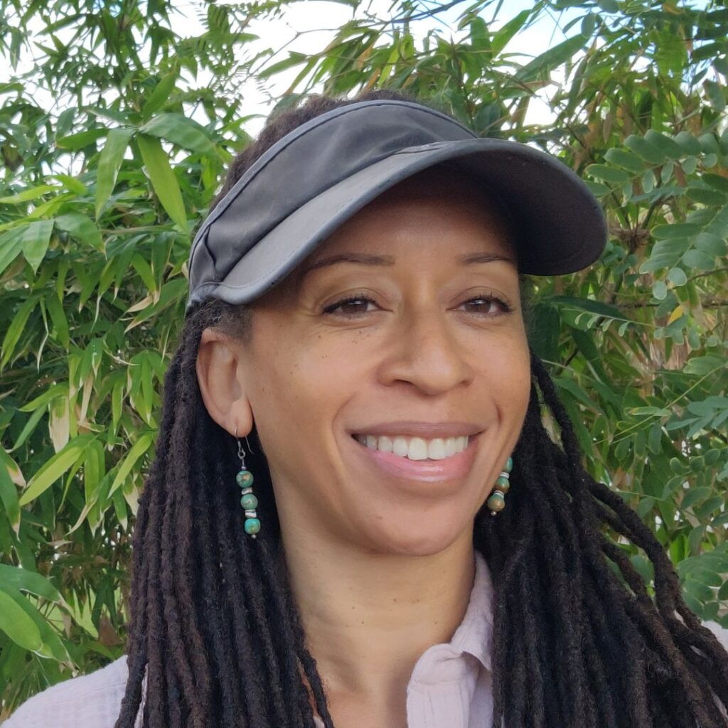 Connie Brittenburg in a grey visor standing in a garden. Connie Brittenburg founder of Calendula's Garden.