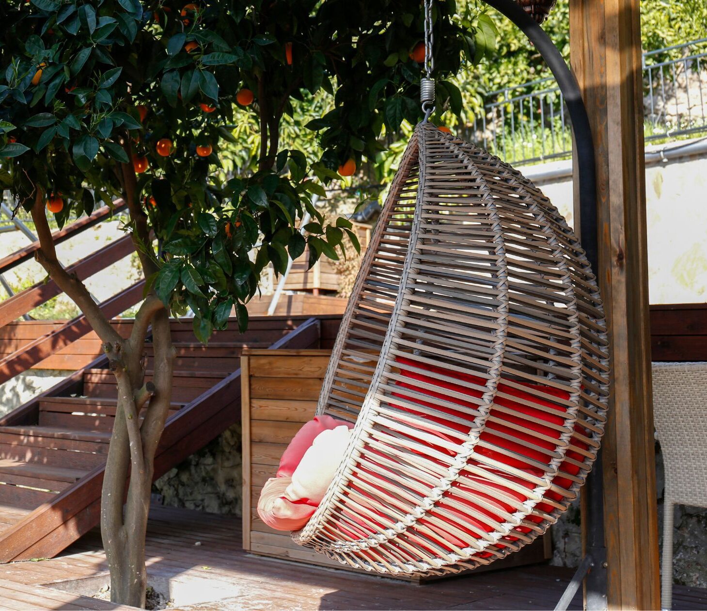 A wicker hanging chair on a patio next to an orange tree.
