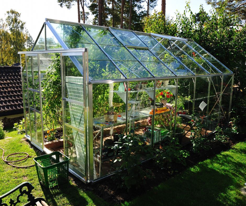 A glass garden greenhouse filled with frost sensitive plants and a potting bench.