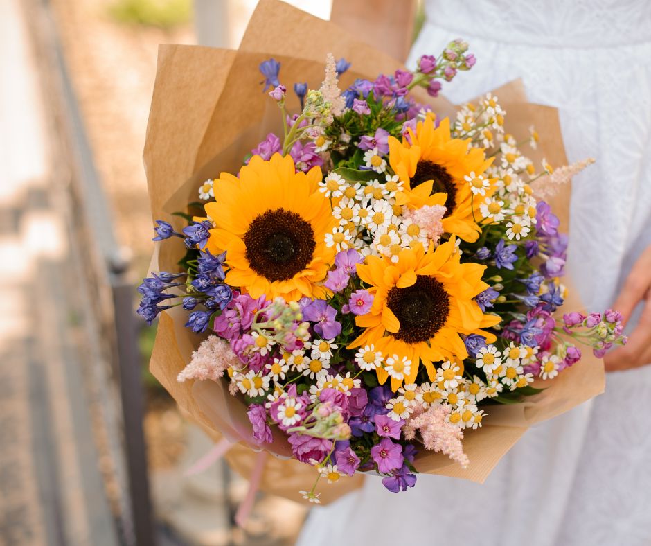 A bright summer bouquet featuring sunflowers, white, pink, and purple flowers.