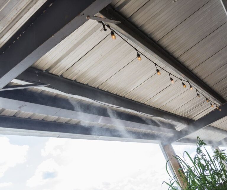 A patio misting system installed on a metal overhang with lights.