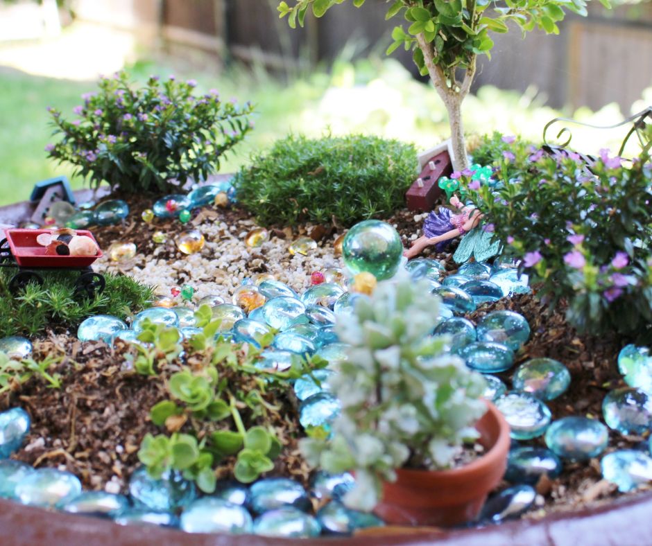 A shallow tray with moist soil, pebbles, plants and tiny toys.